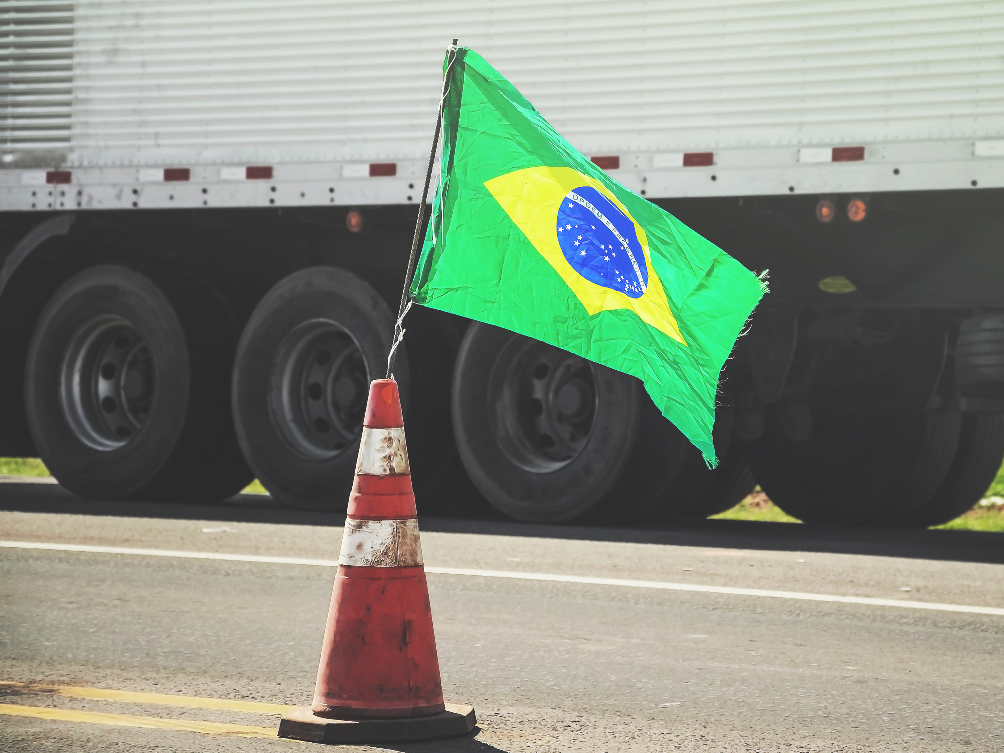 Brazilian flag on a red traffic cone of a highway with a blurred truck on background